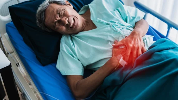 Elderly man lying in a hospital bed, grimacing in pain and clutching his stomach